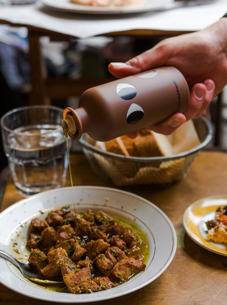 a bottle of yiayia black truffle infused olive oil is being poured on top of a plate of stew