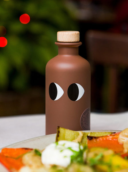 a bottle of yiayia black truffle infused olive oil sits on a table behind a salad