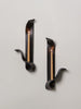 two black ceramic wall sconces resembling ribbons hold lit beeswax tapers on a white wall