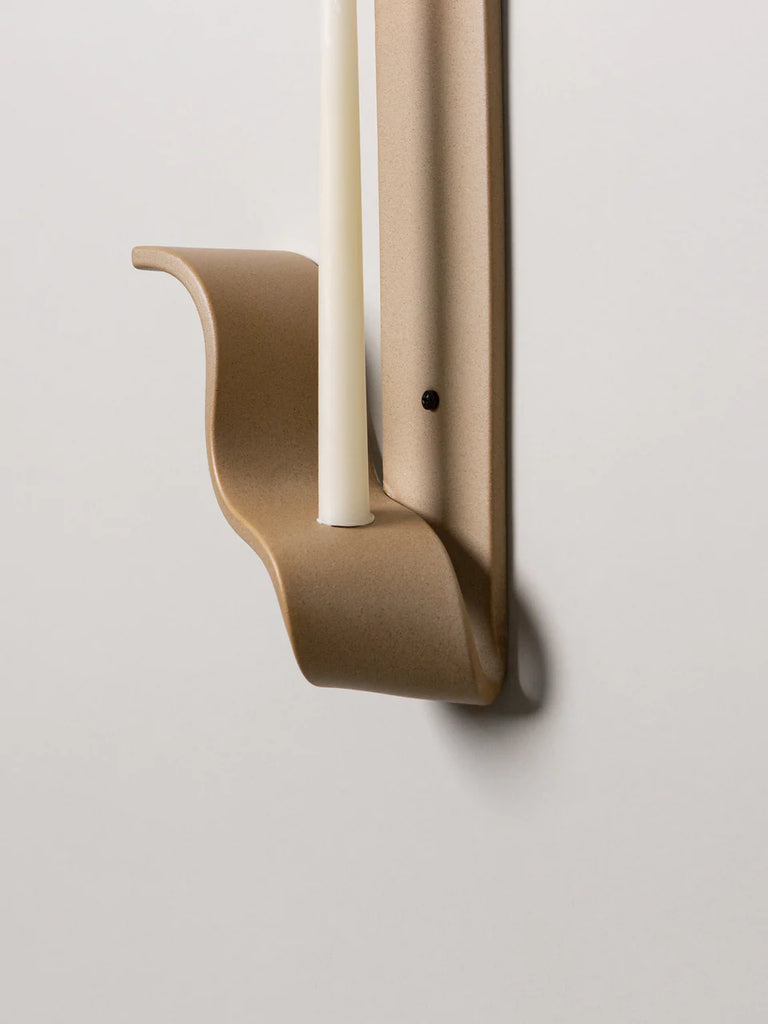detail of a tan ceramic wall sconce resembling a ribbon made by sin ceramics holds a lit beeswax taper on a white wall