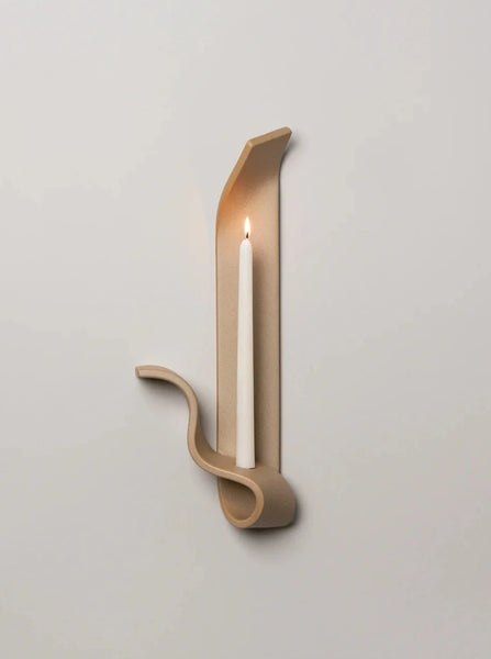 a tan ceramic wall sconce resembling a ribbon made by sin ceramics holds a lit beeswax taper on a white wall