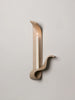 a tan ceramic wall sconce resembling a ribbon made by sin ceramics holding a lit taper  on ta white wall