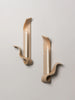 two tan ceramic wall sconces resembling ribbons made by sin ceramics hold lit beeswax tapers on a white wall