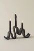 black ceramic candelabra shaped like a ribbon with 3 lit candle tapers on a white background