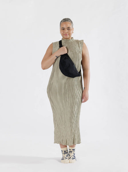 woman carrying a black crescent shaped nylon fanny pack with a black front zipper and black strap made by Baggu over her shoulder against a white background