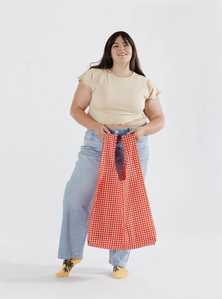 woman wearing a shirt and jeans holding a red gingham reuseable baggu big bag against a white background