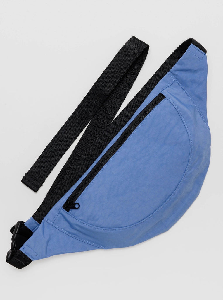 A pansy blue crescent shaped nylon fanny pack with a black front zipper and black strap made by baggu against a white background