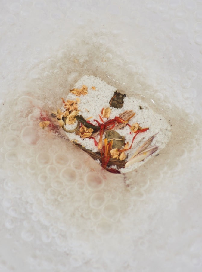 An even keel bath fizzy/shower steamer with dried yellow, red, and green botanicals fizzing and bubbling in water 