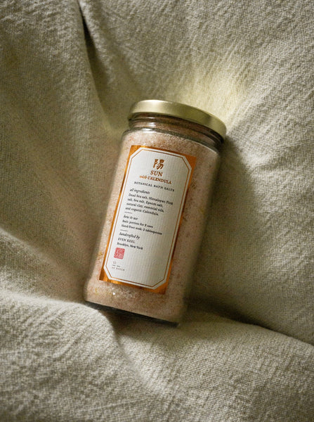 Even Keel sun bath salts in glass jar against a beige fabric background