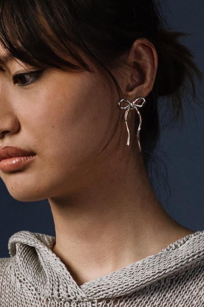 Woman wearing silver bow earrings by Kara Yoo against a dark background 