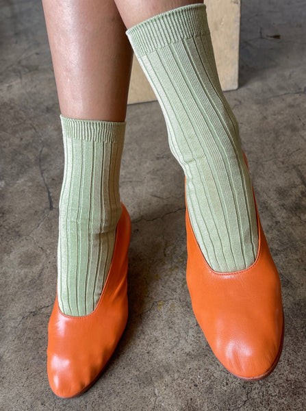 A person wearing avocado green le bon shoppe her socks with orange flats 