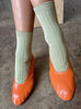 A person wearing avocado green le bon shoppe her socks with orange flats 