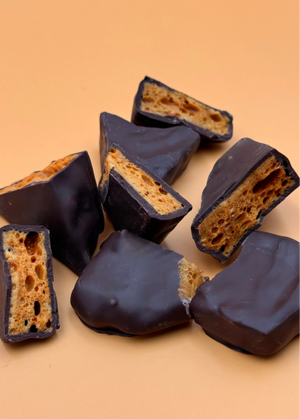 Chocolate-covered honeycomb candy pieces on a beige background