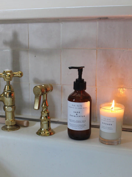 a bottle of na nin sage and eucalyptus hand wash sitting on a bathroom sink beside a lit candle 