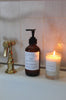 a bottle of na nin sage and eucalyptus hand wash sitting on a bathroom sink beside a lit candle 