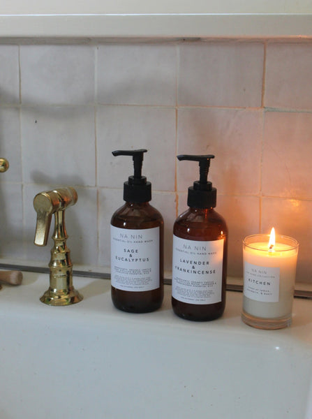 two bottles of na nin essential oil hand wash beside a lit candle in a bathroom