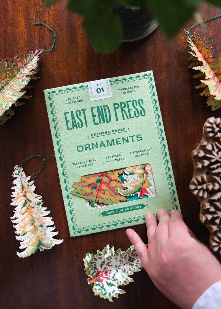Handmade paper ornaments with 'East End Press' packaging on a wooden surface.