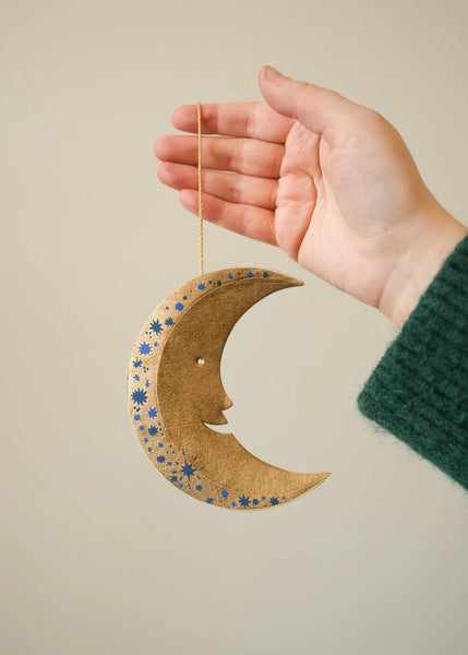 Hand holding a decorative moon-shaped ornament with a beige background