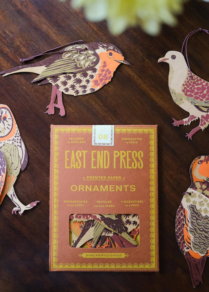 Box of East End Press ornaments with decorative bird cutouts on a wooden surface